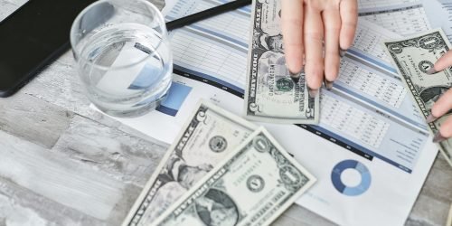 pexels-photo-7735785-7735785 A top view of financial documents with dollar bills and a glass of water, emphasizing budgeting.